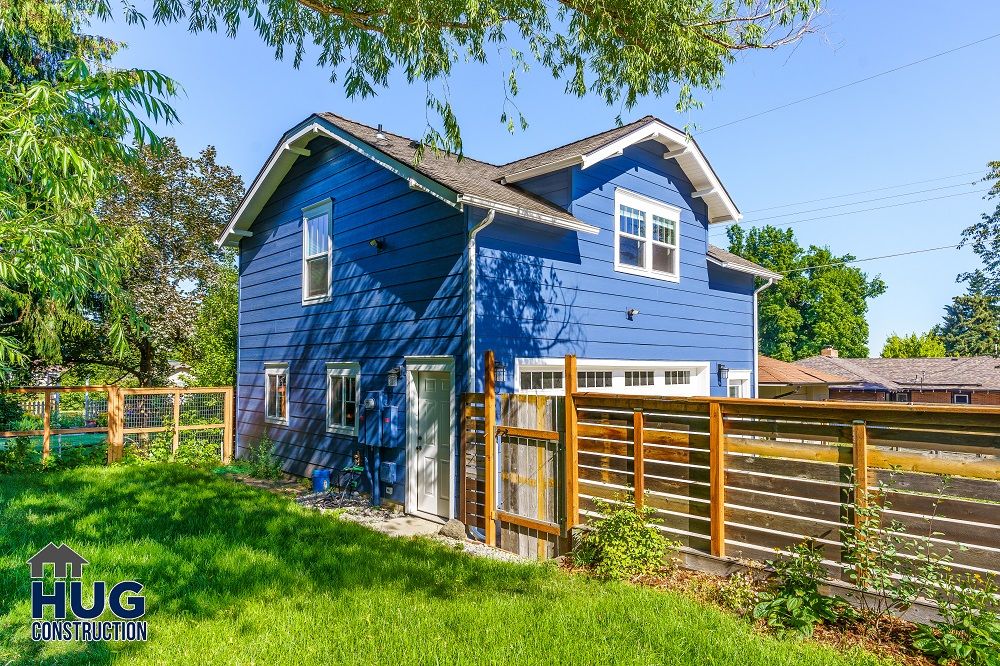 Blue two-story suburban house with an Accessory Dwelling Unit and a wooden fence on a sunny day.