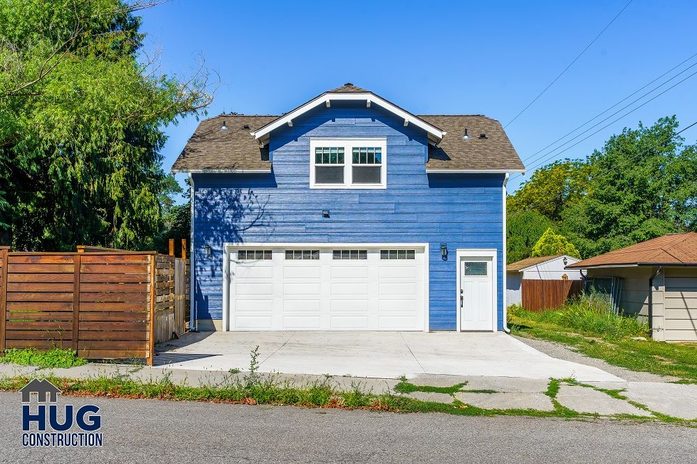 Newly constructed blue two-story house with a white garage door and an Accessory Dwelling Unit, set against a clear sky.