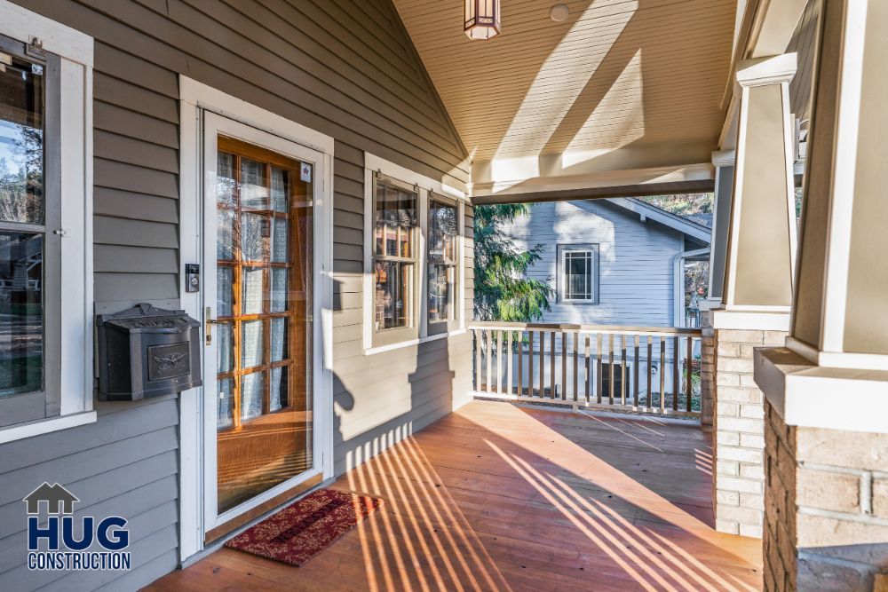 Sunlit wooden porch of a residential home, recently enhanced with remodels and additions, featuring a glass-paneled door and a railing.