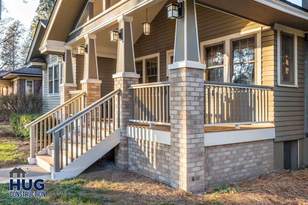 Newly constructed home porch with stone pillars and wooden railings, featuring recent remodels and additions, at dusk.