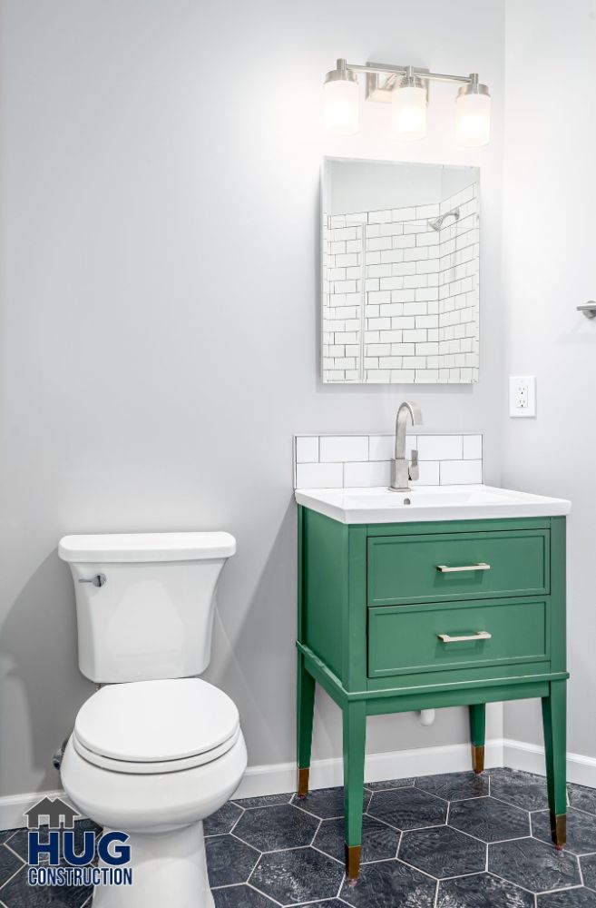 Modern bathroom interior, including remodels and additions, with white walls, a green vanity cabinet, and a toilet under bright lights.