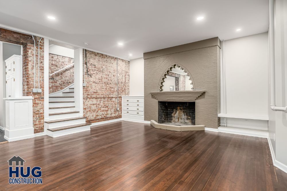 Renovated room featuring polished hardwood floor, exposed brick wall, white fireplace, staircase, and additions.