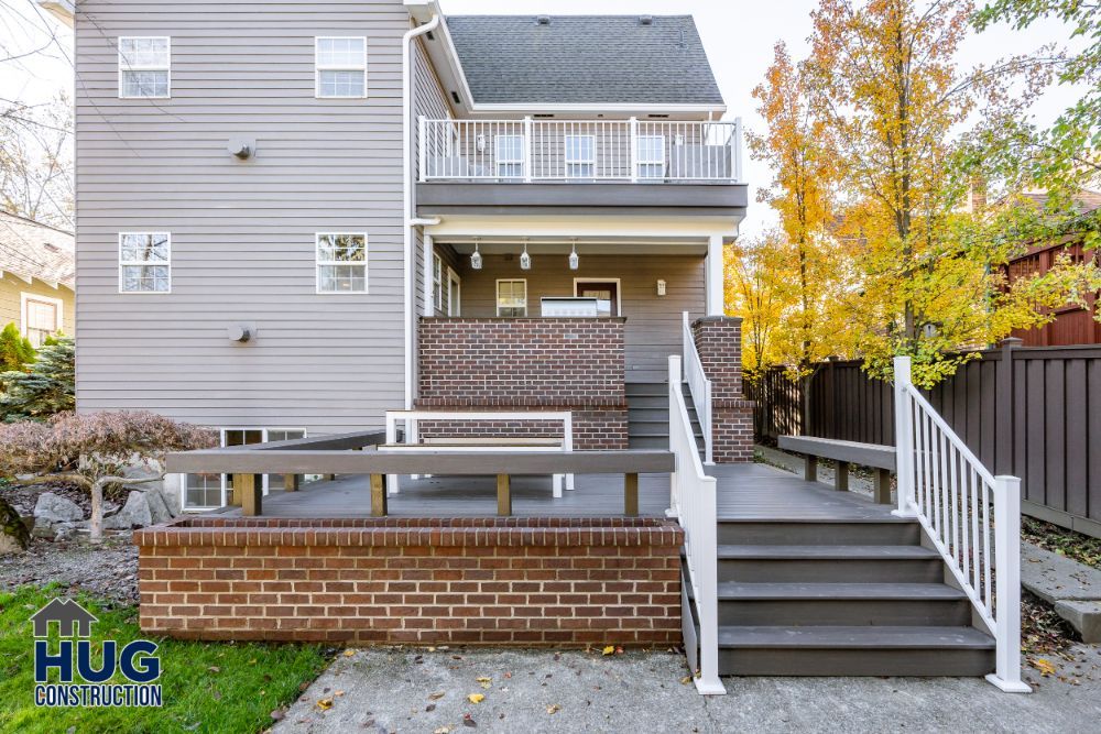 Newly constructed residential deck and staircase remodels, leading to a two-story house with autumn foliage in the background.
