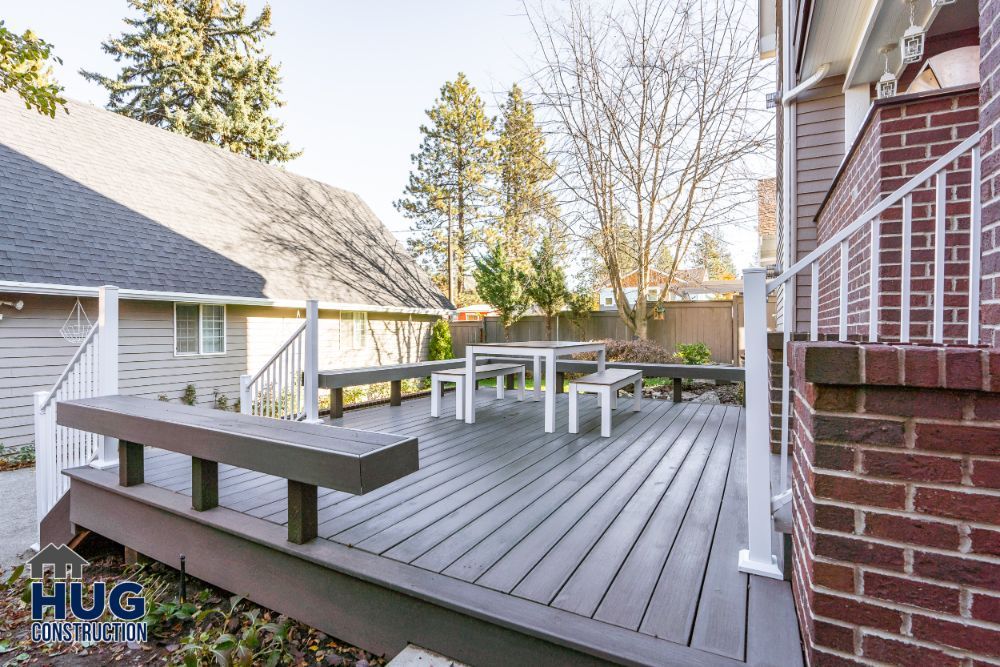 Spacious wooden deck remodels attached to a brick house with patio furniture and a fenced yard.