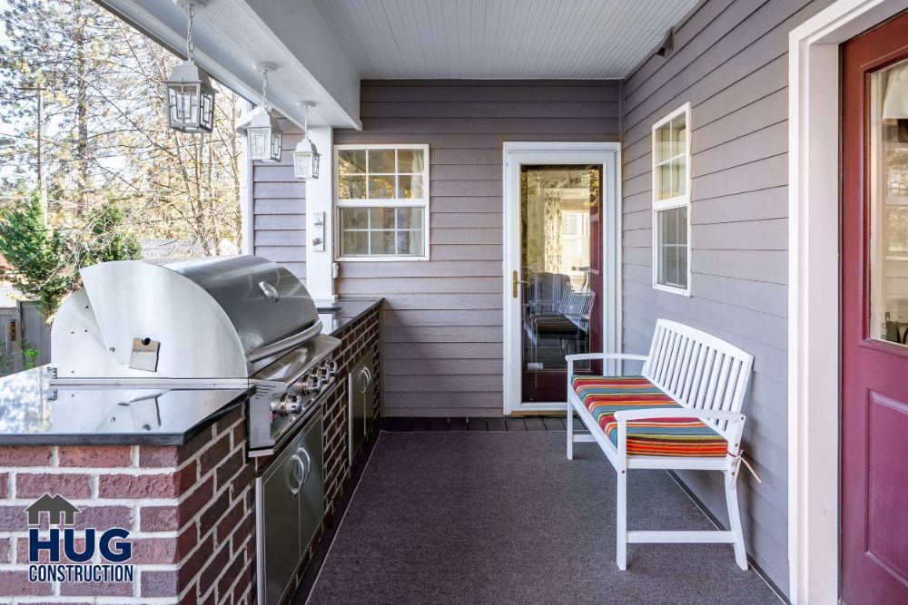 A cozy residential porch featuring remodels and additions, including a grill and a bench with a colorful cushion.
