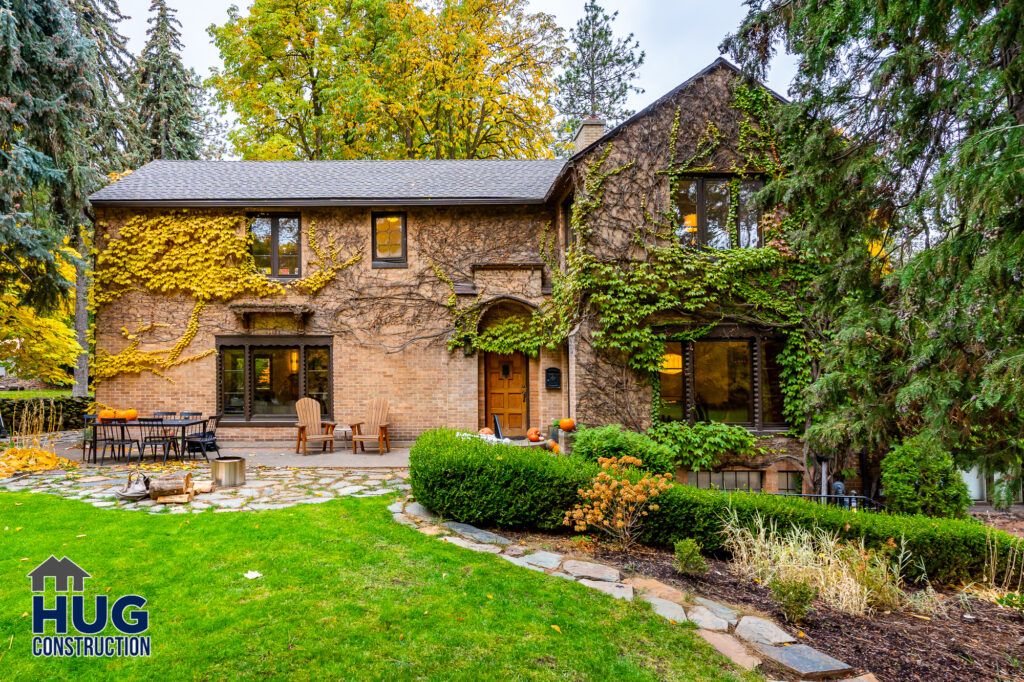 Two-story brick house with ivy on the exterior walls, featuring a stone patio and surrounded by lush greenery, mature trees, and an interior remodel.