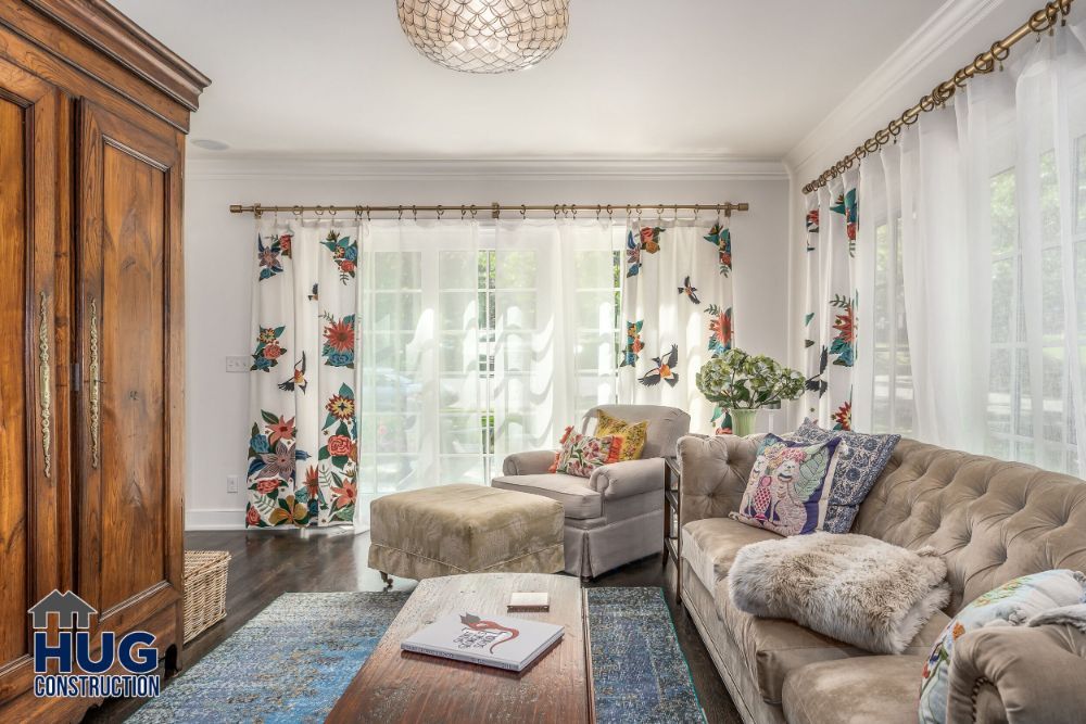 A cozy living room with a combination of traditional and modern decor elements, featuring a comfortable seating area with patterned curtains and a hardwood floor, thoughtfully updated with tasteful remodels and additions.