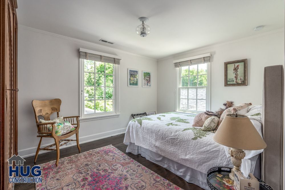 A tidy and well-lit bedroom, recently remodeled with a bed, wooden chair, side table, and colorful rug.