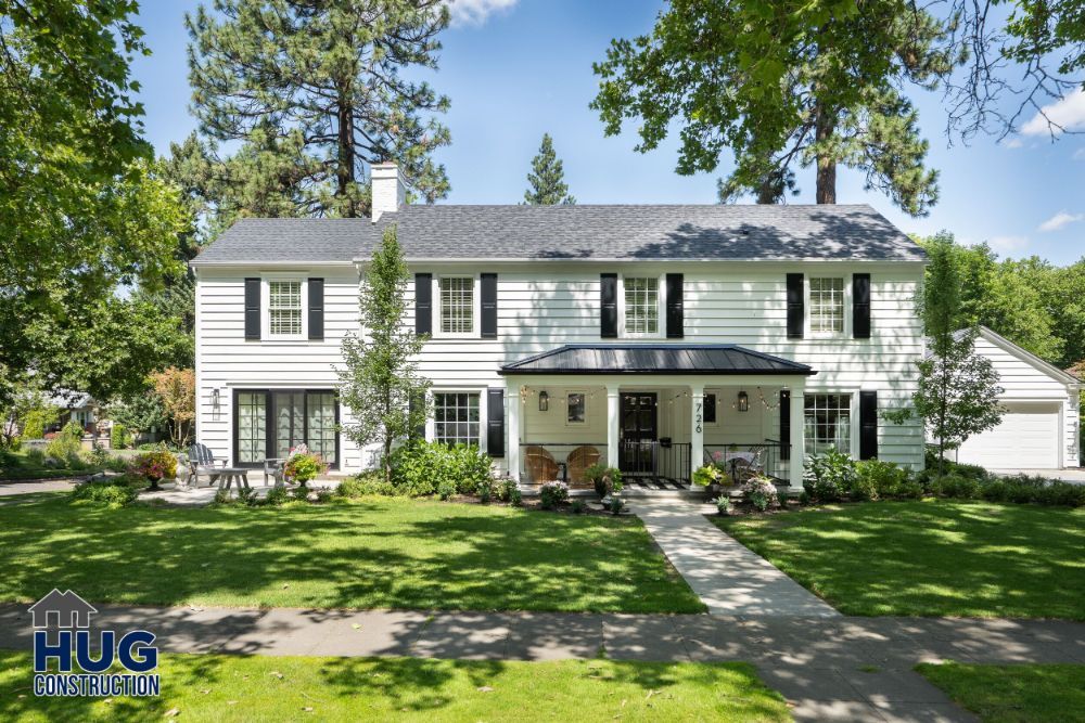 Two-story white suburban house with remodels and additions, featuring a well-manicured lawn and trees.