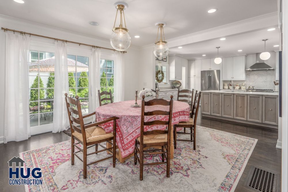 An elegant dining room seamlessly connected to a modern kitchen, featuring a wooden table set, ornate rug, stylish lighting fixtures, and recent remodels and additions.