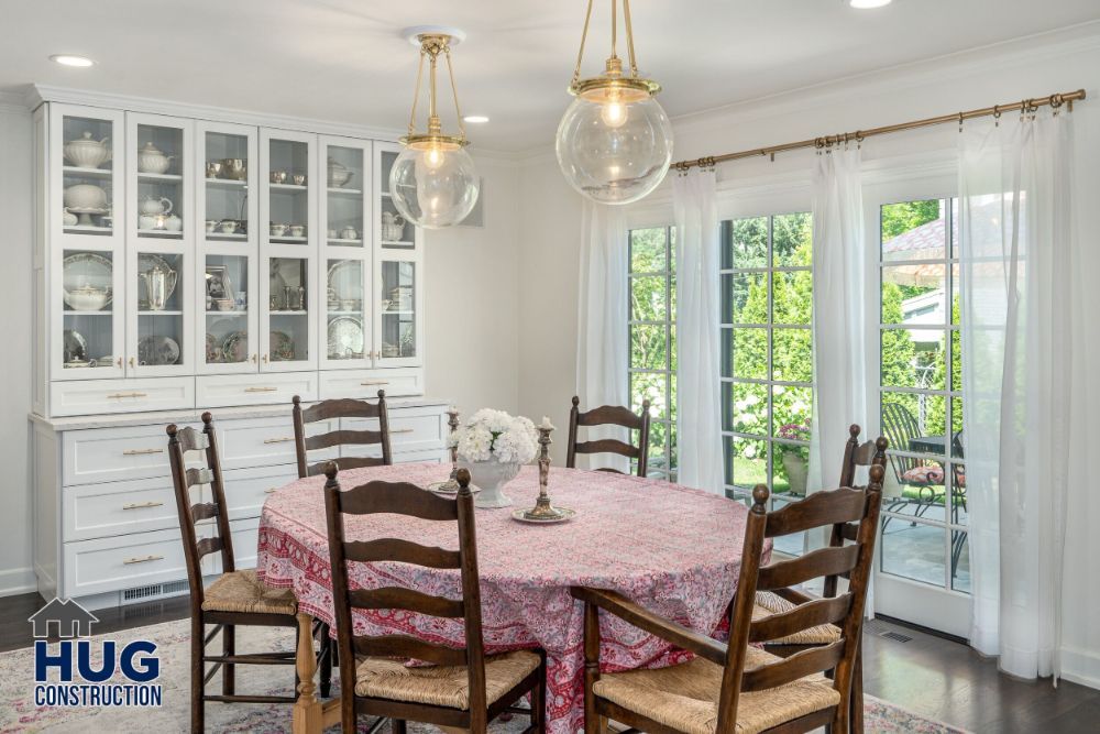 Elegant dining room remodels with a wooden table set, glass-fronted white cabinets, and pendant lighting.