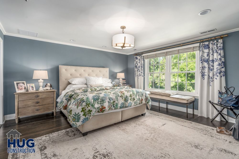Elegantly furnished bedroom with serene color scheme, featuring remodels and additions such as a tufted headboard, floral bedding, and a window seat.