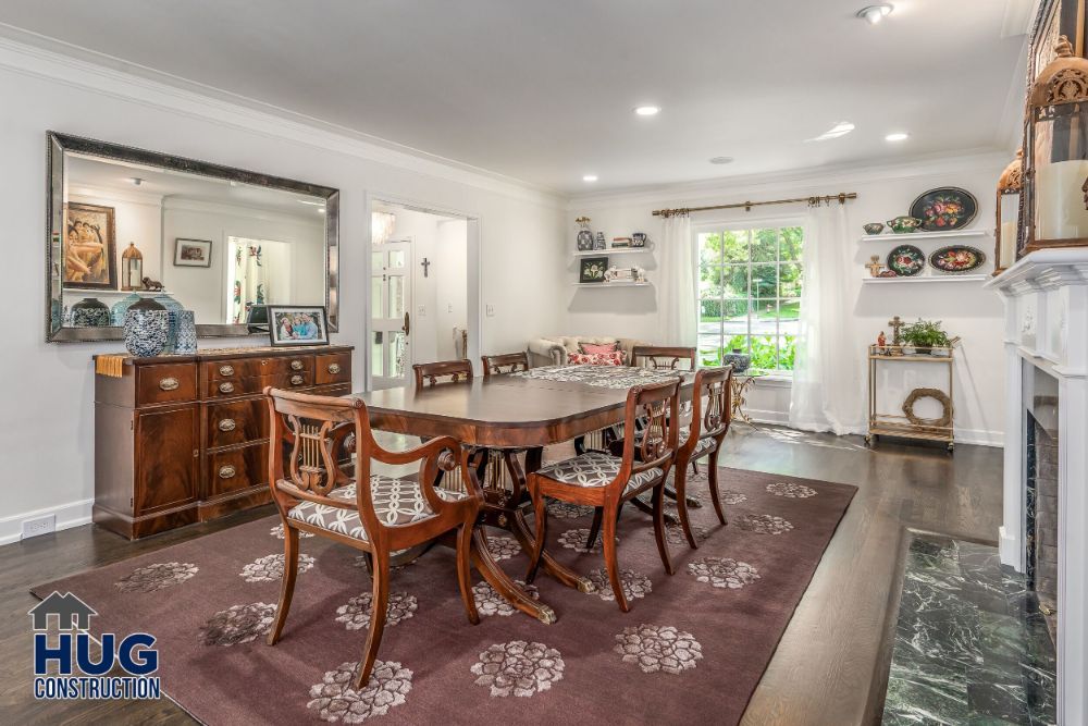 Elegant dining room remodels featuring a wooden table set, large mirror, and a fireplace, with a decorative rug overlaying a polished floor.