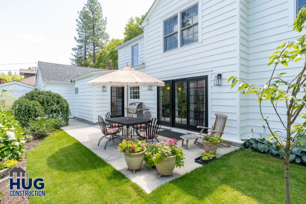 White suburban house with remodels and additions, featuring a patio area including outdoor furniture and potted plants.