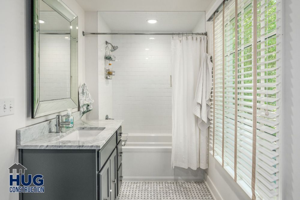 Modern bathroom remodels with white subway tiles, a bathtub with shower, and a vanity with dark countertops.