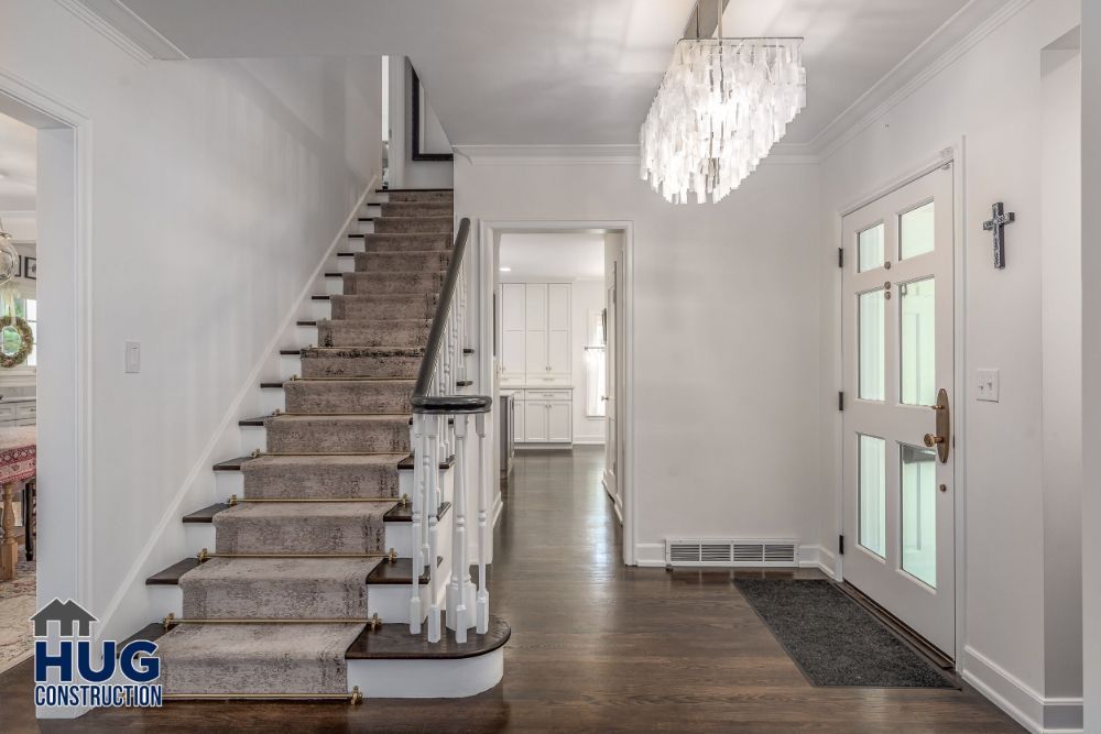 Modern home interior showcasing elegant remodels and additions, including a staircase with white balusters and a crystal chandelier, leading to a bright, welcoming space.