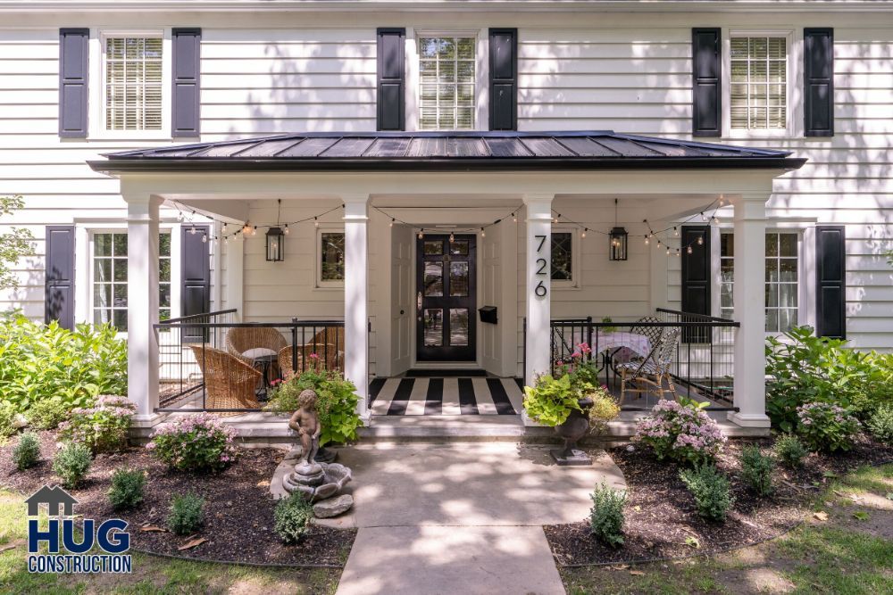 Traditional two-story white house with black shutters, a covered porch with a checkered doorstep, remodels and additions, and a neatly landscaped front yard.