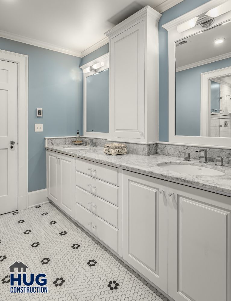 A modern bathroom remodels with white cabinetry, marble countertops, and blue walls.