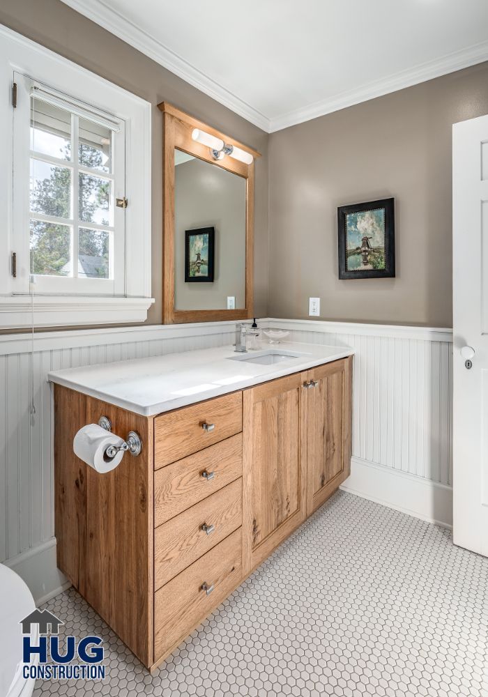 Modern bathroom remodel featuring a wooden vanity with a white countertop, a framed mirror above it, hexagonal floor tiles, and subtle wall artwork.