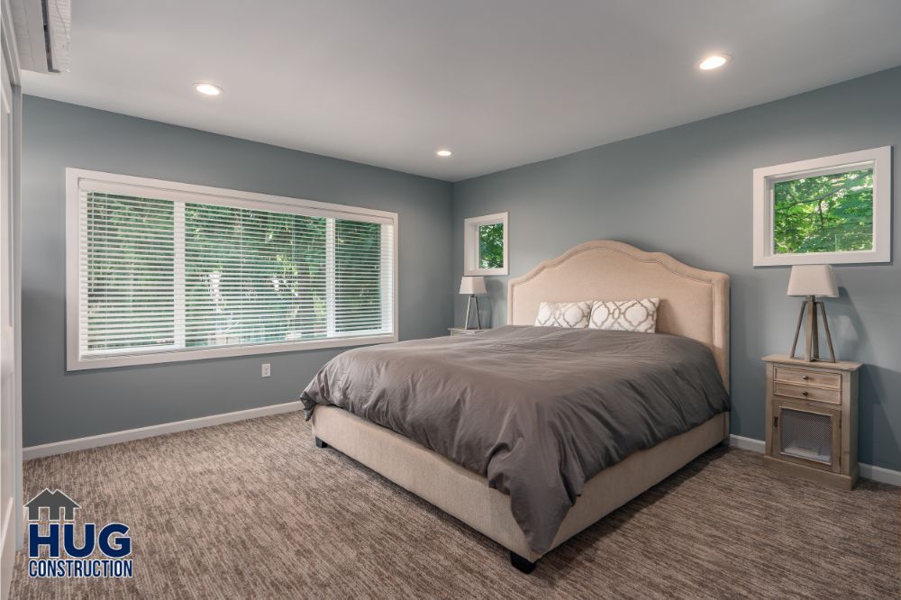 A modern bedroom with a large bed, two windows, gray walls, and recent remodels and additions.