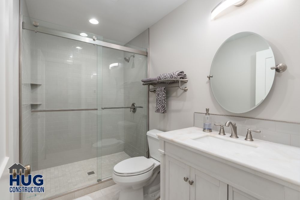 Modern bathroom remodels with a glass shower enclosure, white vanity, and circular mirror.