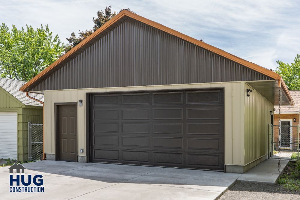 A residential garage with a large dark door and beige exterior walls, specializing in remodels and additions, features a company logo for 
