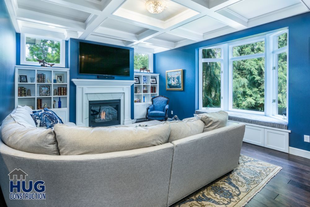 A stylish living room remodel featuring a blue color scheme, with a fireplace, large windows, and a mounted television.