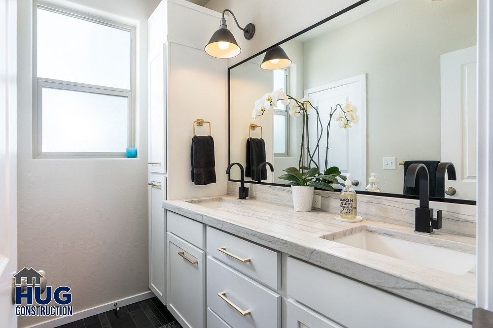 A modern bathroom vanity remodel with a marble countertop, double sinks, and a large mirror flanked by wall sconces.