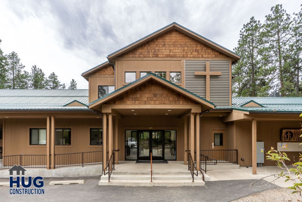 Modern two-story building designed by a prominent commercial contractor in Spokane, with a central entrance and wood siding, surrounded by trees.