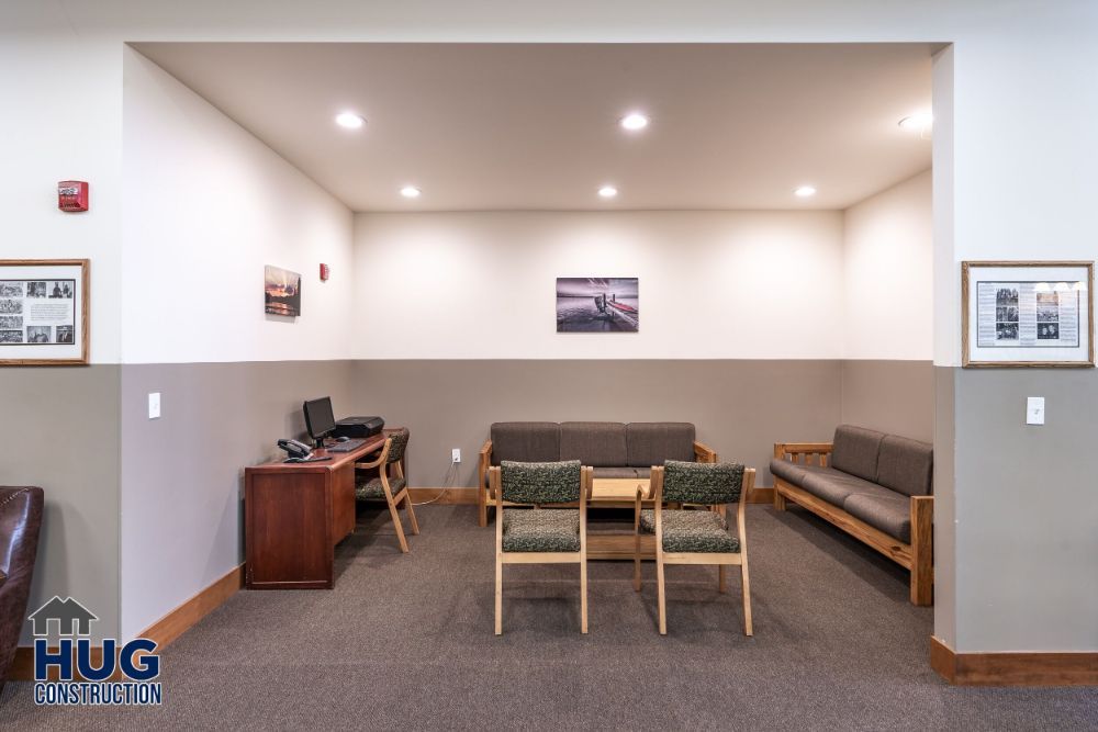 A neat waiting area designed by a Commercial Contractor in Spokane, with chairs, a sofa, a desk with a computer, and framed pictures on the walls.