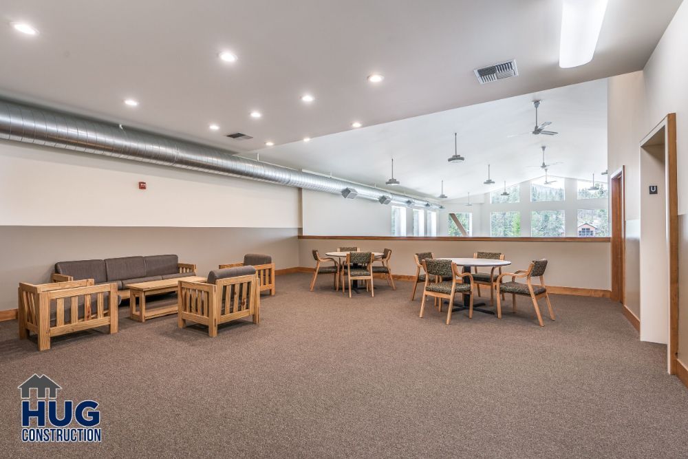Modern community room with tables, chairs, and a seating area, featuring exposed ductwork and neutral tones. Designed by a leading Commercial Contractor in Spokane.
