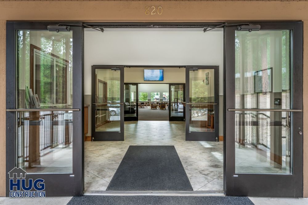 Entrance to a modern building foyer with glass doors, tiled floor, and a logo of Commercial Contractor Spokane construction.