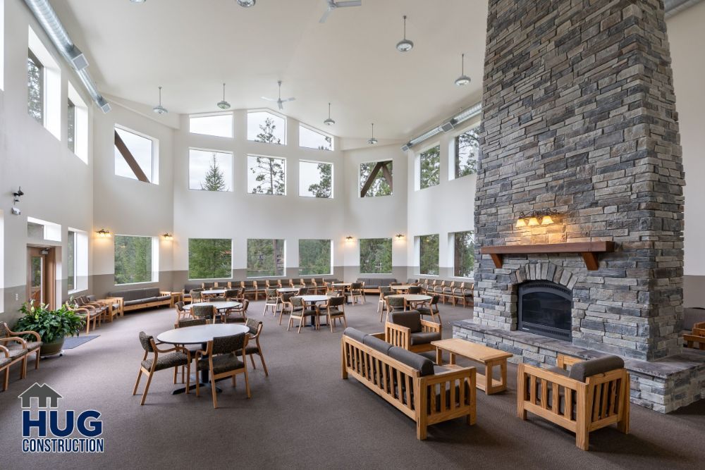 Spacious and serene lounge area with a stone fireplace and comfortable seating under a high ceiling with natural light, designed by a leading Commercial Contractor in Spokane.