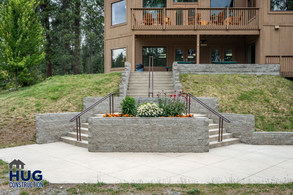 A commercial residential building with stone steps and a landscaped flower bed, featuring a Commercial Contractor Spokane logo in the corner.