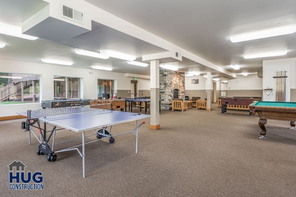 A spacious recreational room designed by a Commercial Contractor Spokane, featuring a ping pong table, pool table, and seating areas with a neutral color scheme and ample lighting.