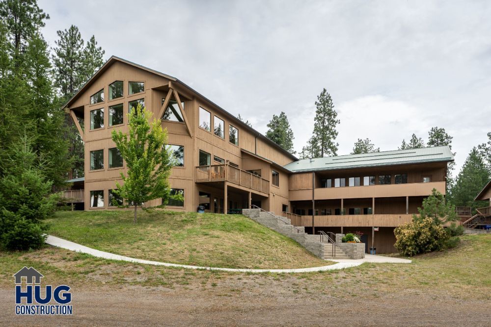 A large modern wooden building designed by a commercial contractor in Spokane, featuring a green roof, multiple levels, and expansive windows, surrounded by a natural landscape.