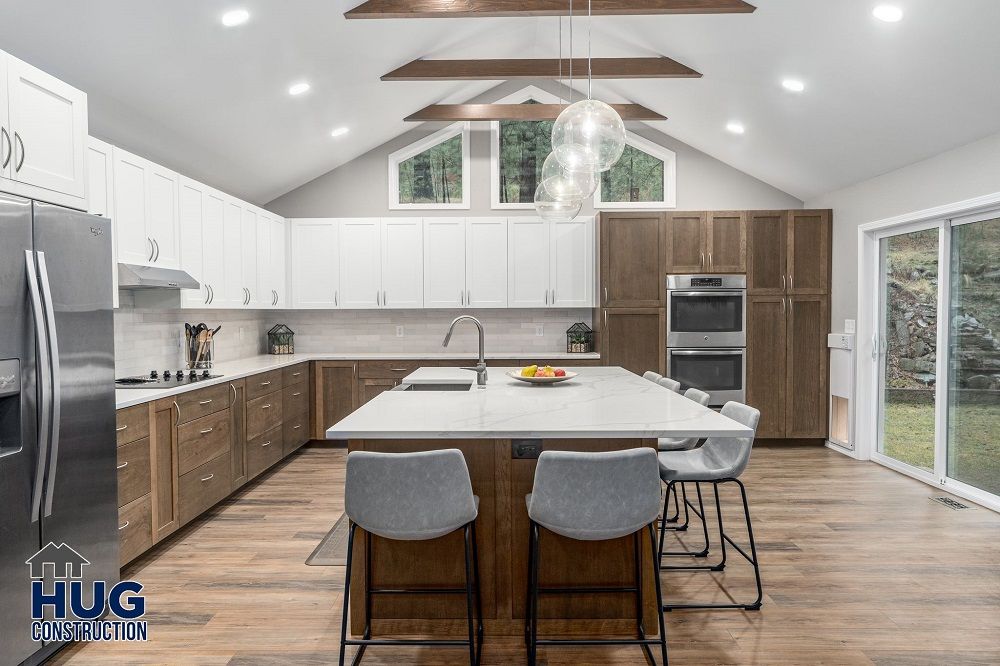 Modern kitchen interior remodels with white and wood cabinetry, stainless steel appliances, and a central island with bar stools.