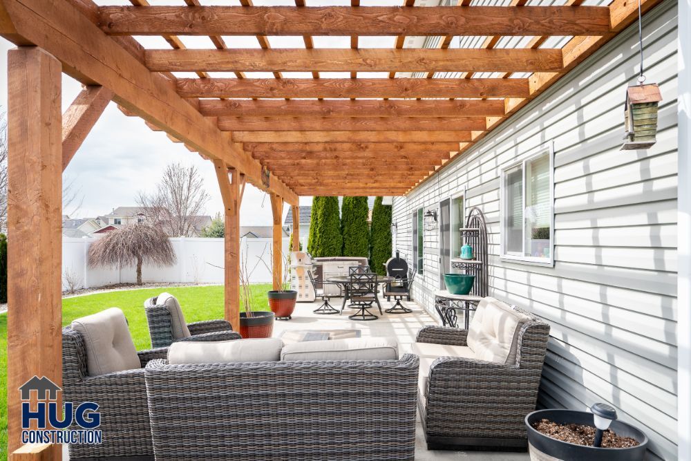 A cozy backyard patio with a wooden pergola, outdoor furniture, recent remodels and additions, and a neatly maintained lawn.