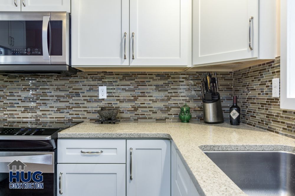 Modern kitchen interior with white cabinets, granite countertops, and a mosaic tile backsplash, featuring new remodels and additions.