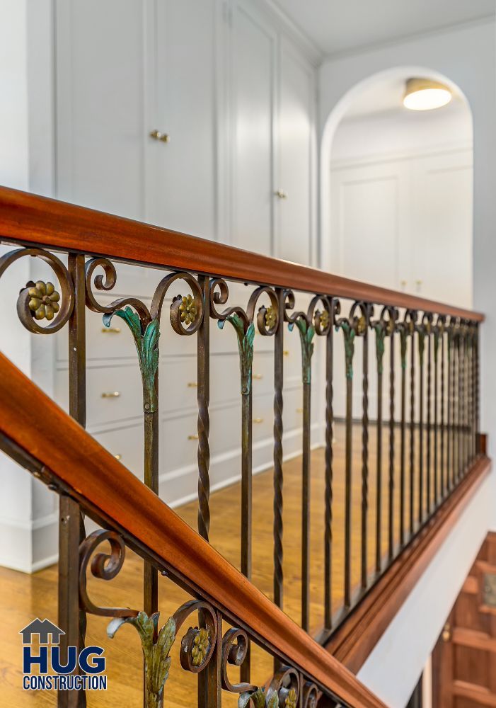 Elegant wooden banister with decorative metal balusters in a hallway, featuring a logo for 'hug construction' specializing in remodels and additions.
