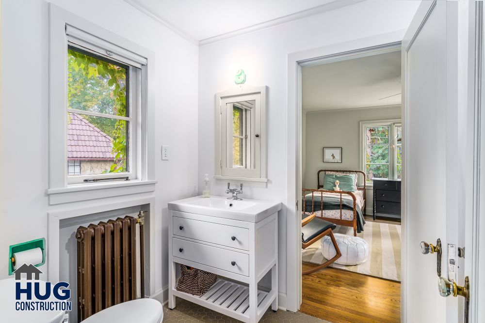 A bright, clean bathroom with a white vanity, the result of recent remodels, leads to an adjoining bedroom visible through an open door.