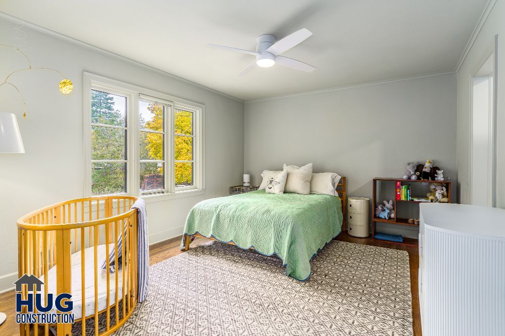 Brightly lit bedroom, recently remodeled, with a double bed, ceiling fan, and a baby crib.
