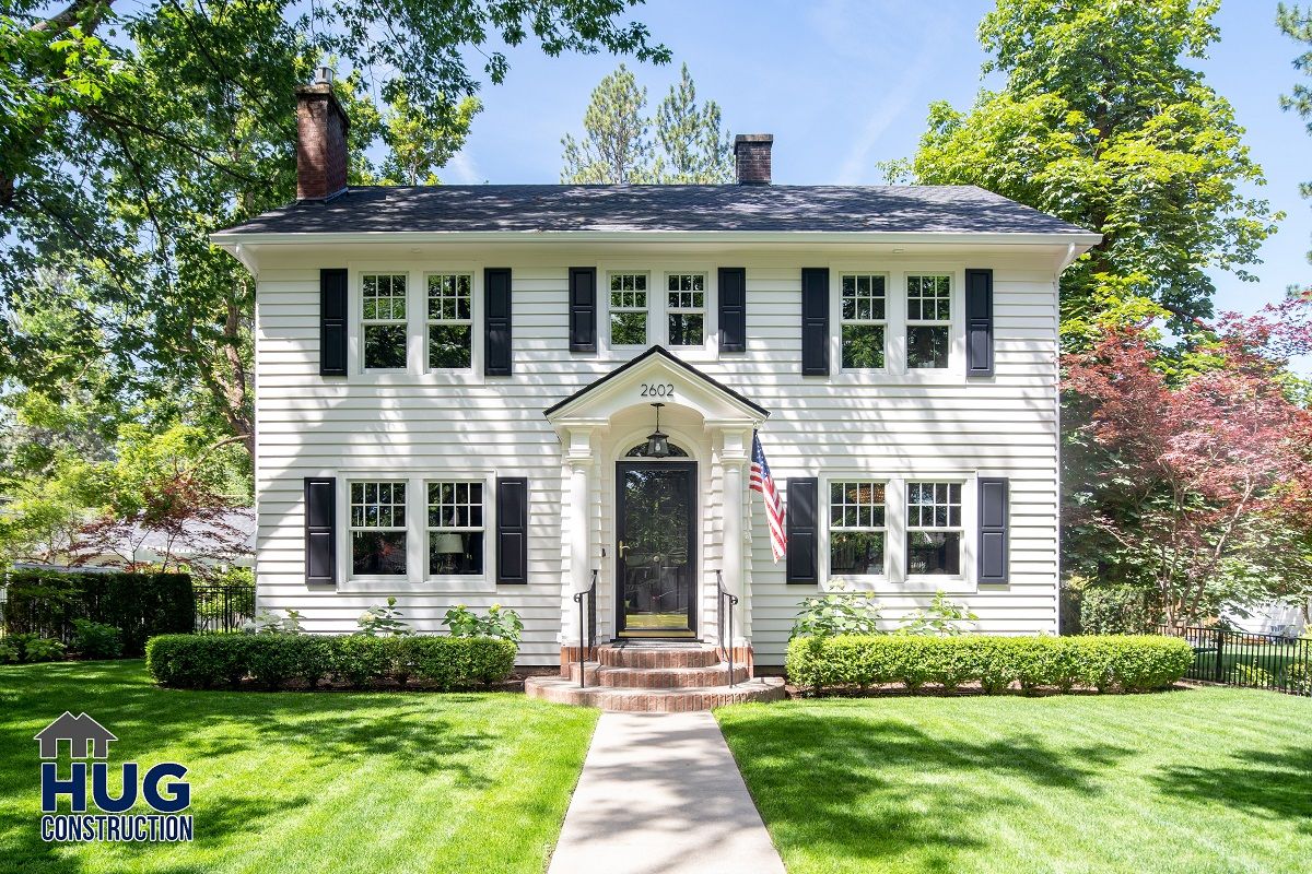 Two-story white colonial house with remodels, additions, green lawn, and trees.