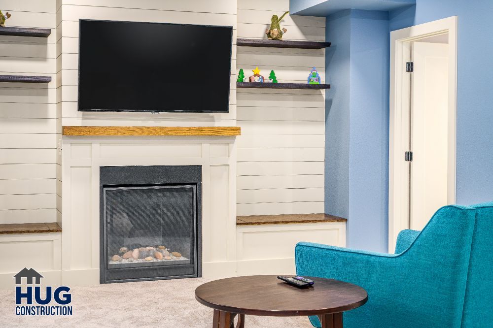 A modern living room featuring a mounted television above a fireplace, with built-in shelving and additions such as a blue sofa.
