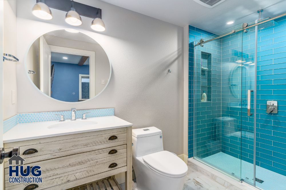Modern bathroom remodels with blue tile shower, white fixtures, and wooden vanity.