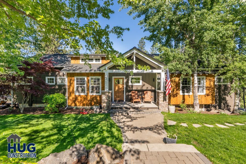 A single-story suburban house, featuring remodels and additions, with a well-kept lawn, a stone pathway, and an American flag displayed on the front.