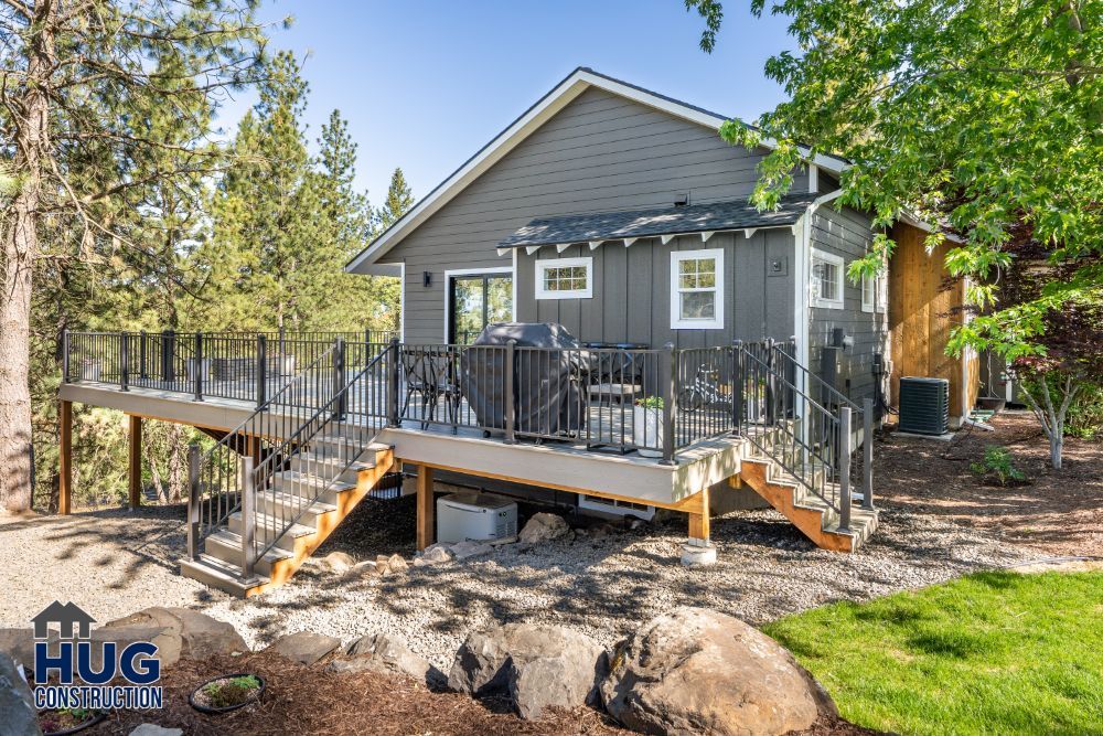 A modern house with remodels and additions, including an elevated deck and staircase, surrounded by a natural landscape.