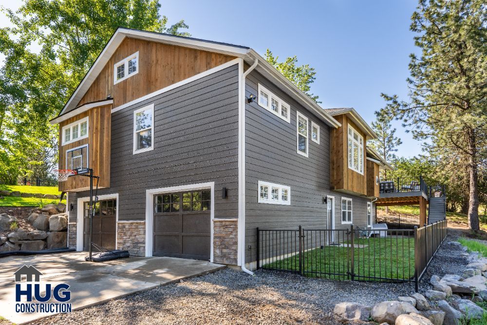 Two-story house with a mix of wood and vinyl siding, featuring remodels, an attached garage, and a fenced yard on a landscaped hillside.