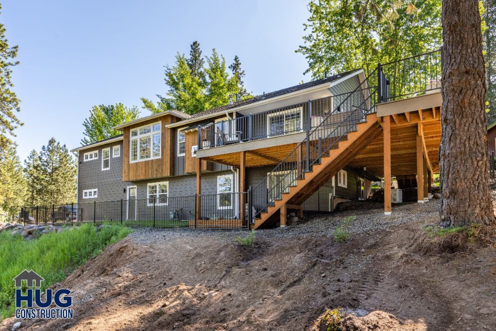 Two-story house with remodeled wooden deck and stairs in a forested area.