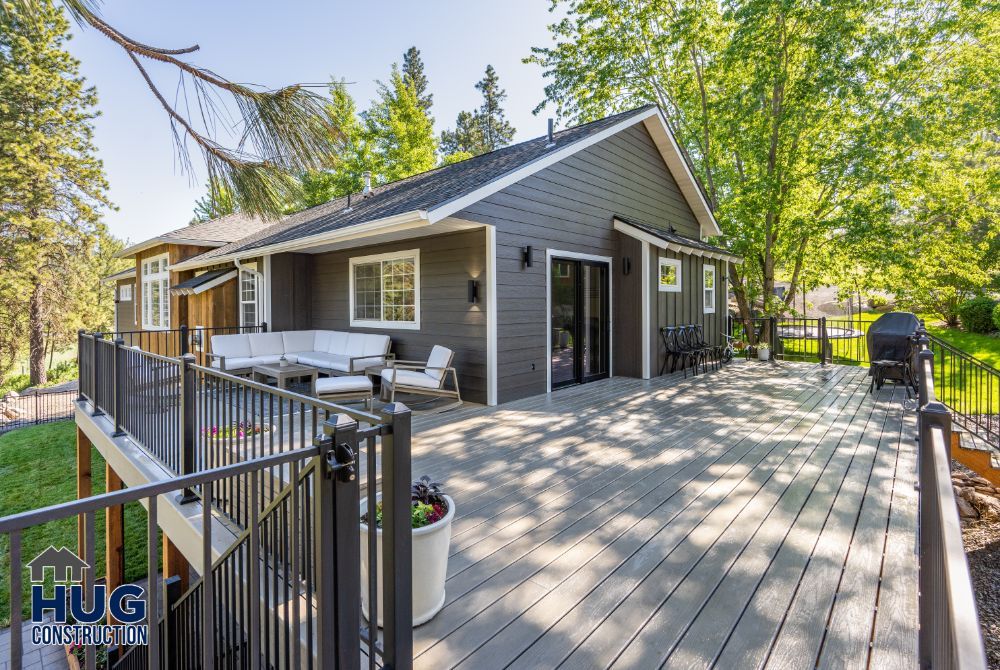 A modern single-story house with remodels, featuring a spacious wooden deck and outdoor seating area surrounded by greenery.
